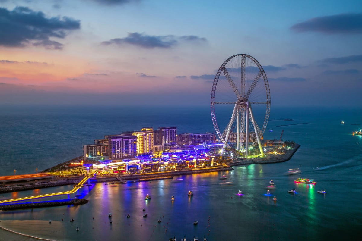 Ain Dubai and the Bluewaters waterfront lit up under a pink evening sky, boats moored offshore