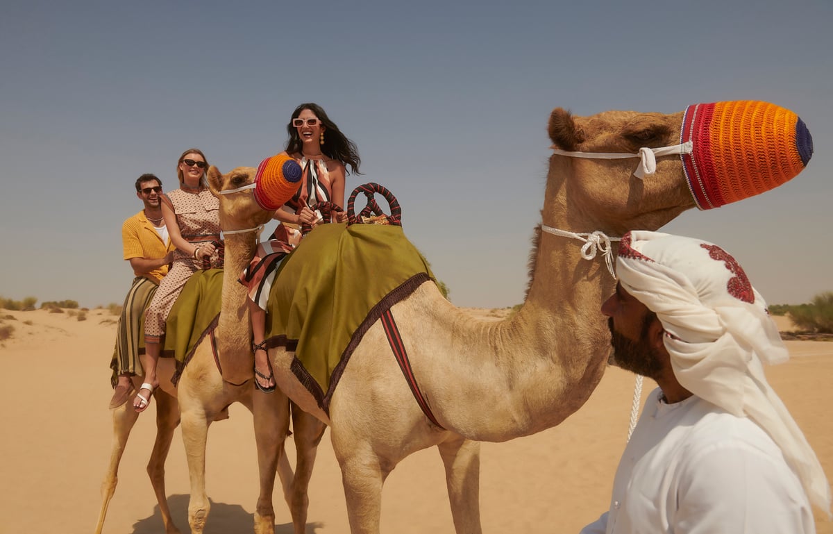 Guests laughing on a camel led by a guide in a white ghutra