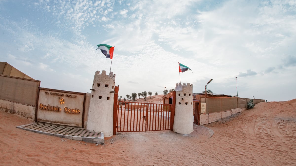 The fort-style gates of Bedouin Oasis camp beneath UAE flags and a big sky