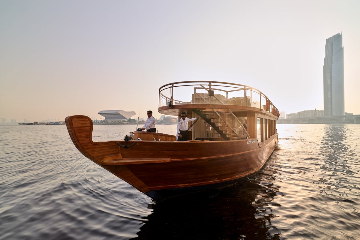 A traditional wooden dhow gliding across the creek with the city's towers behind