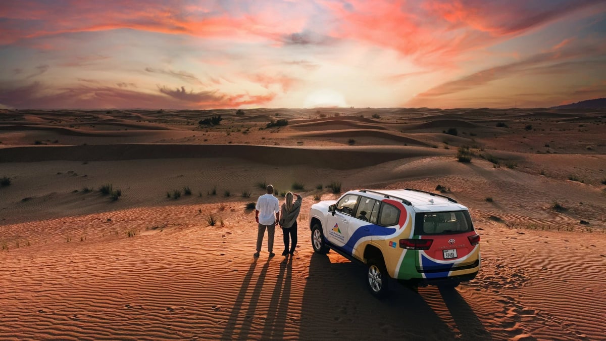 Guests standing beside a four-by-four on a ridge of red dunes at a fiery sunset