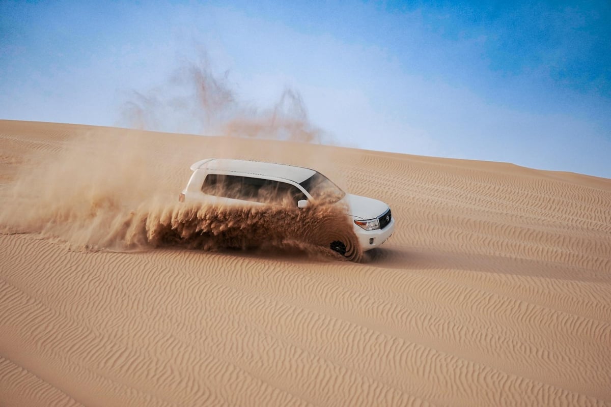 A white four-by-four throwing up a plume of sand on a dune