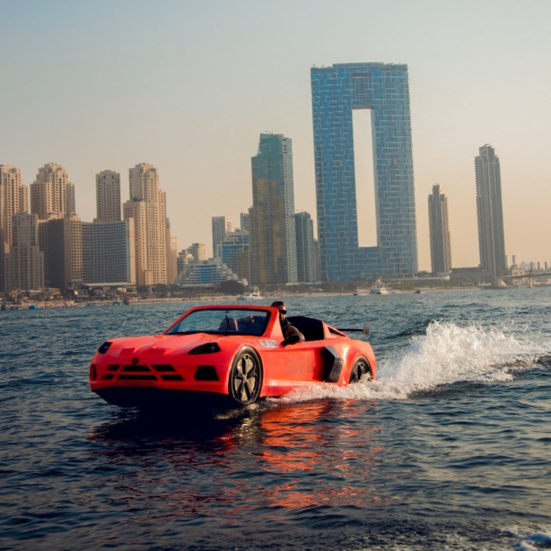 A red jet car speeding across the marina with the city's towers behind
