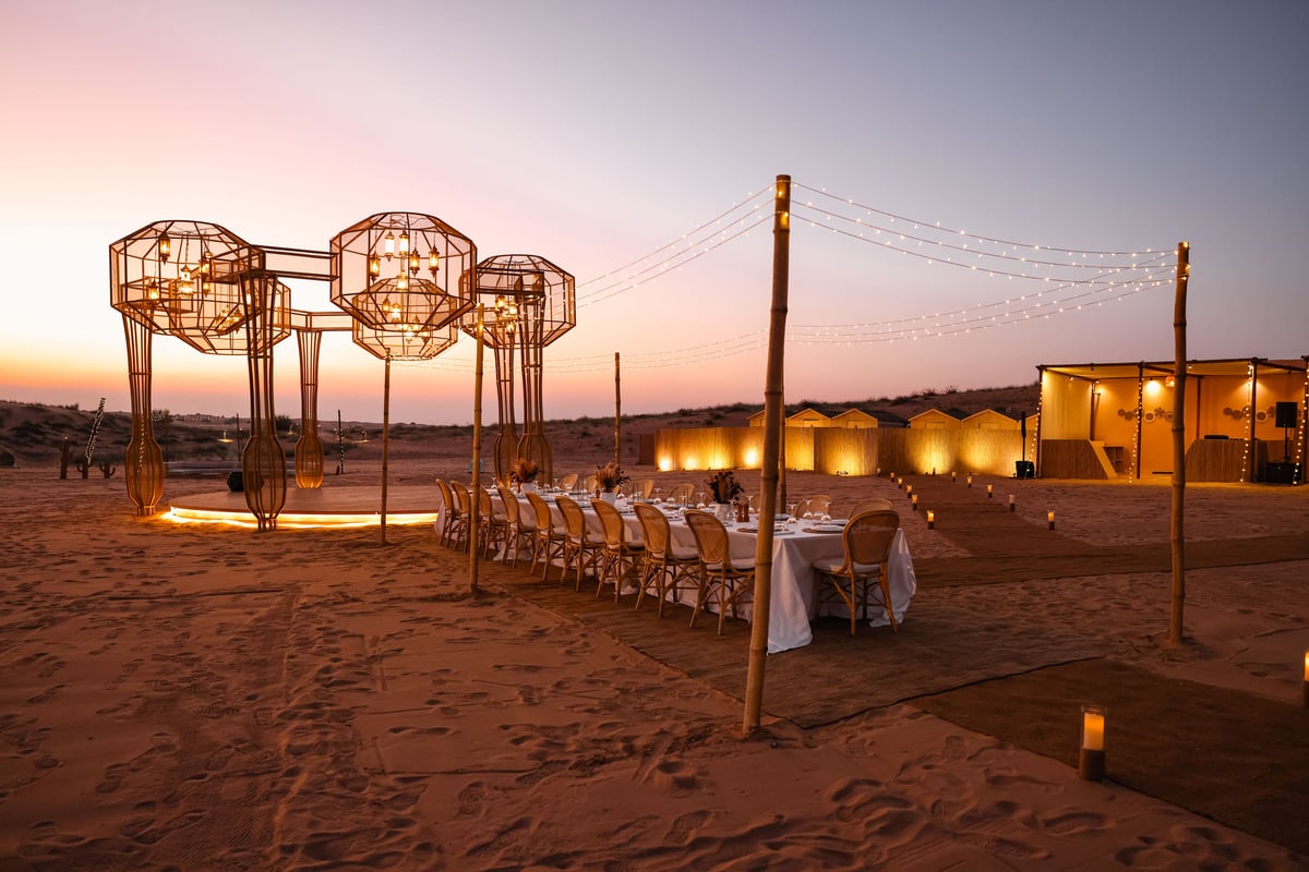 A long table set beneath rattan lanterns in the desert at sunset