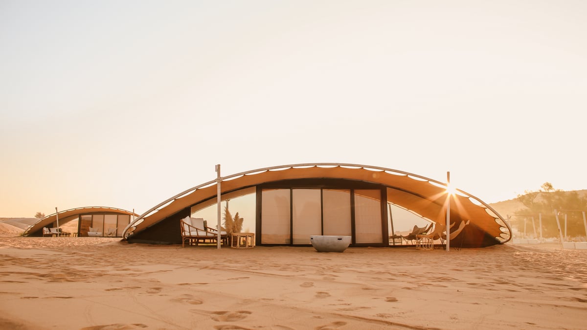 Two curved suites on the dunes at sunset with their glass fronts glowing