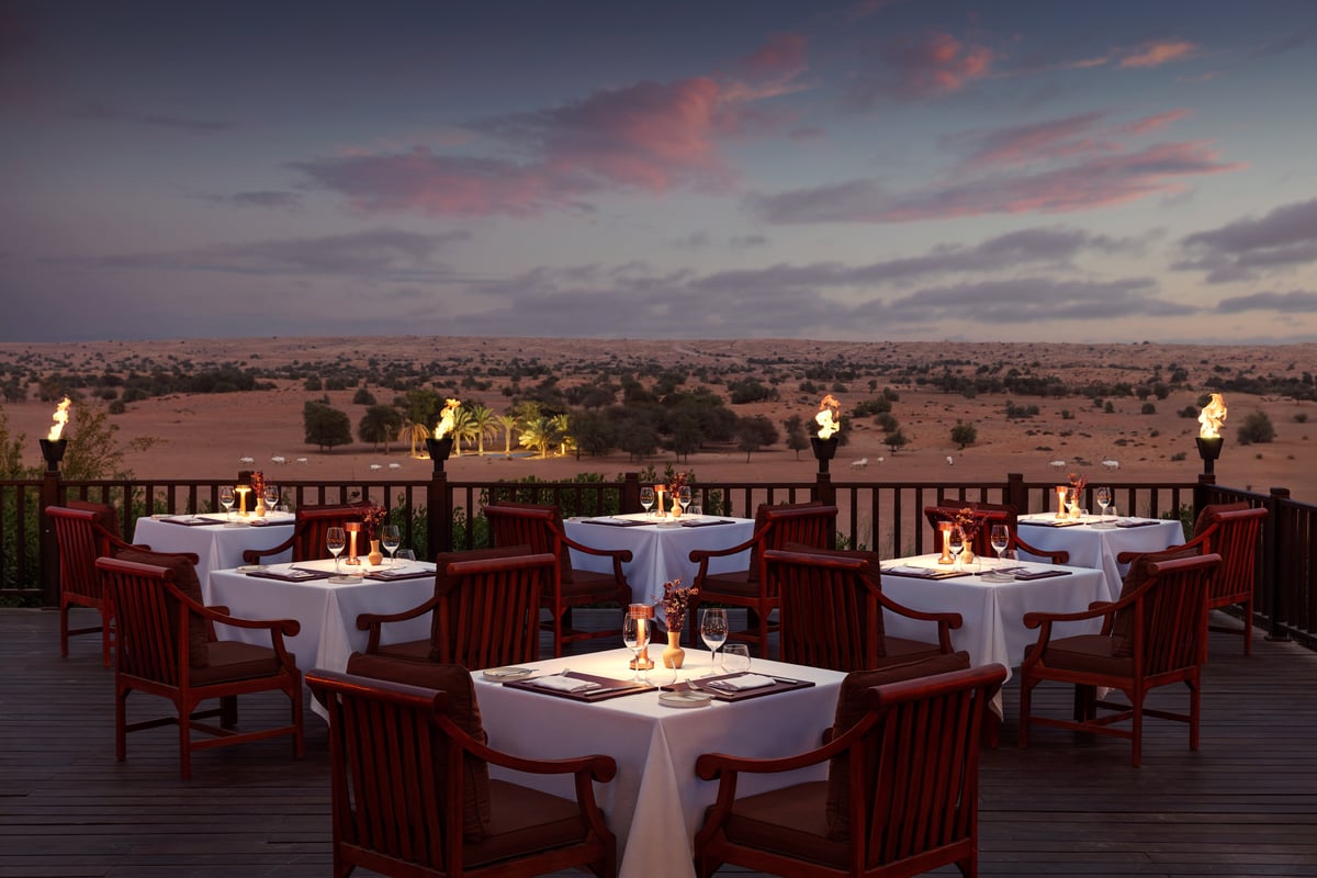Al Diwaan terrace at Al Maha with candlelit tables and flaming torches overlooking the open desert at dusk.