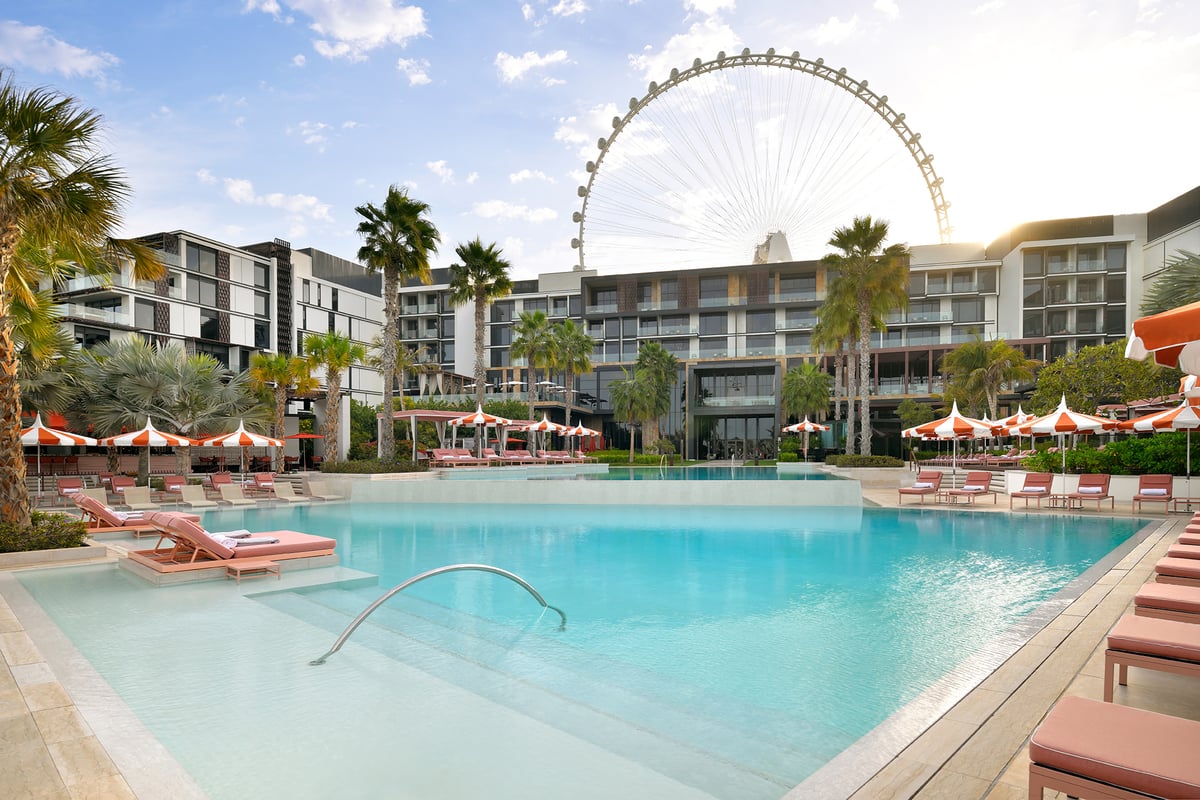 The main pool at Banyan Tree Dubai with pink loungers, striped umbrellas and Ain Dubai rising behind the hotel.