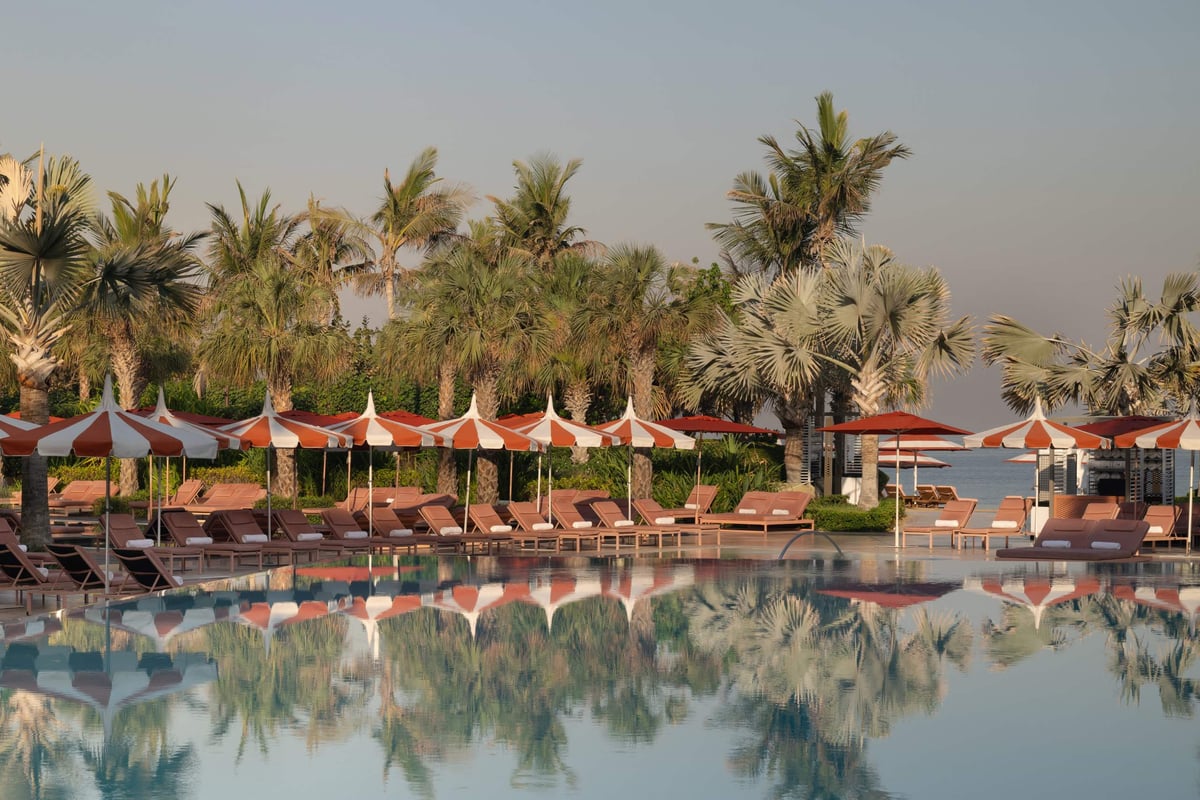 Rows of loungers and red-and-white umbrellas reflected in the pool at Banyan Tree Dubai at dusk.