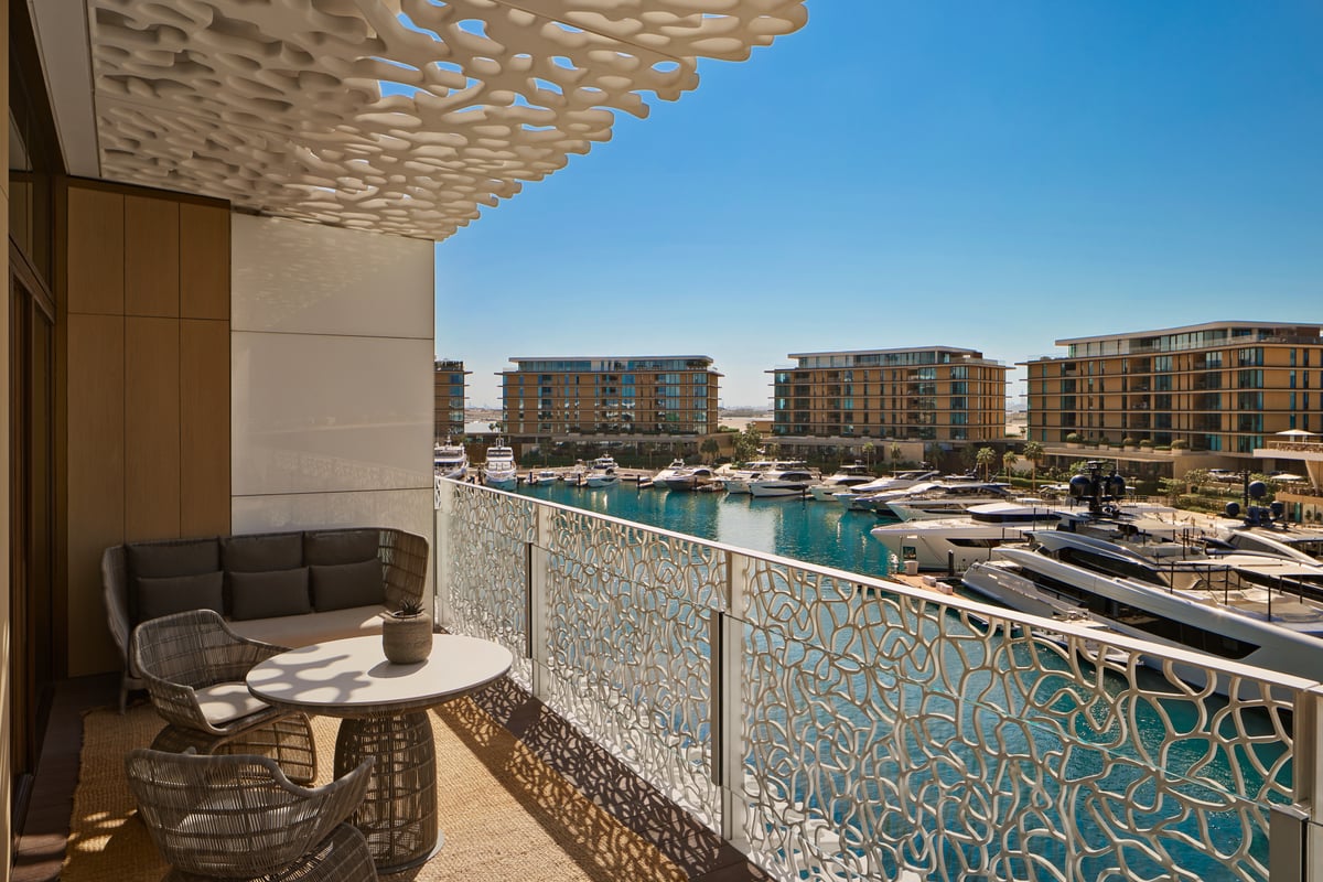 A guest room balcony at the Bvlgari Resort Dubai with woven chairs behind a lattice rail, overlooking the yacht marina.
