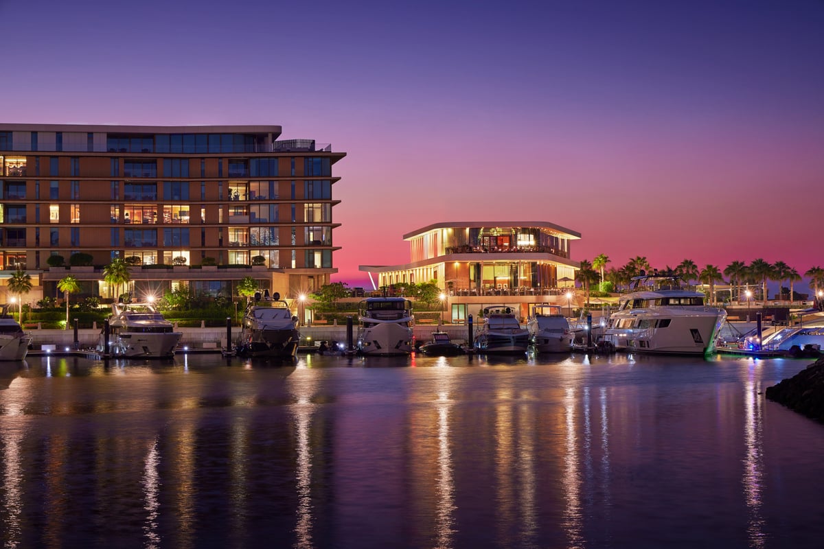 The Bvlgari Resort Dubai marina at night, with lit residences and yachts reflected in the still water under a pink sky.