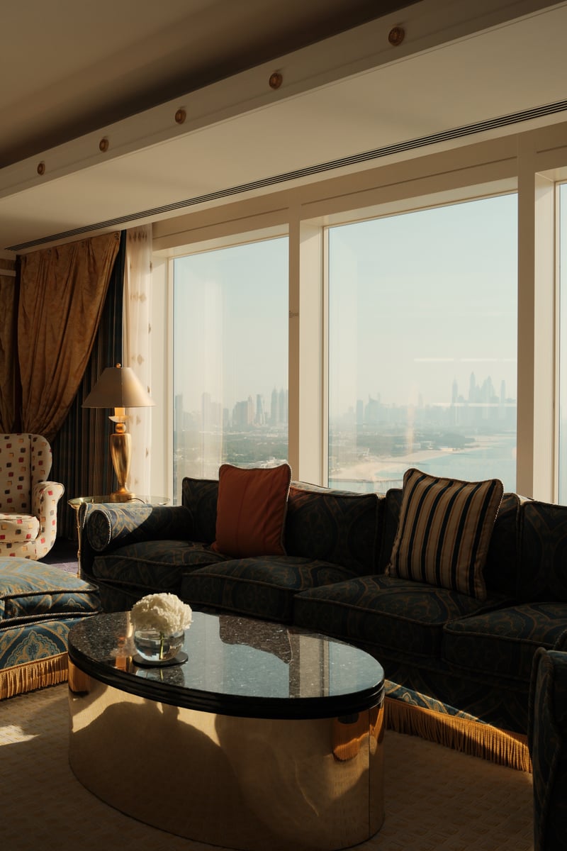 Suite living room with a dark sofa and glass coffee table before a wide window over Dubai