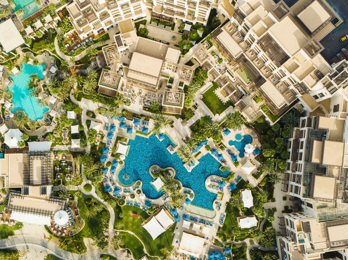 Top-down aerial of Jumeirah Al Naseem's curving pools, palm gardens and white rooftops.