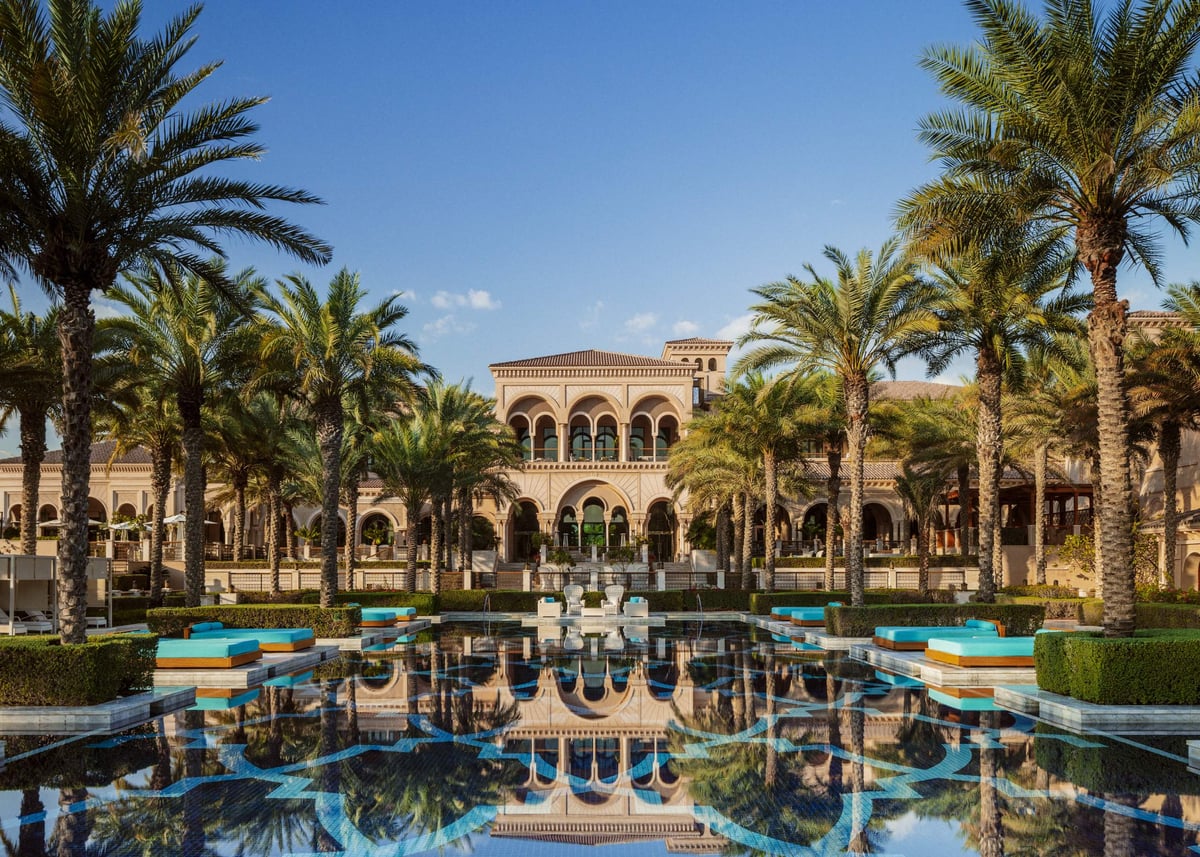 The Grand Pool at One&Only The Palm, with blue loungers and palms reflected in front of the Manor House.