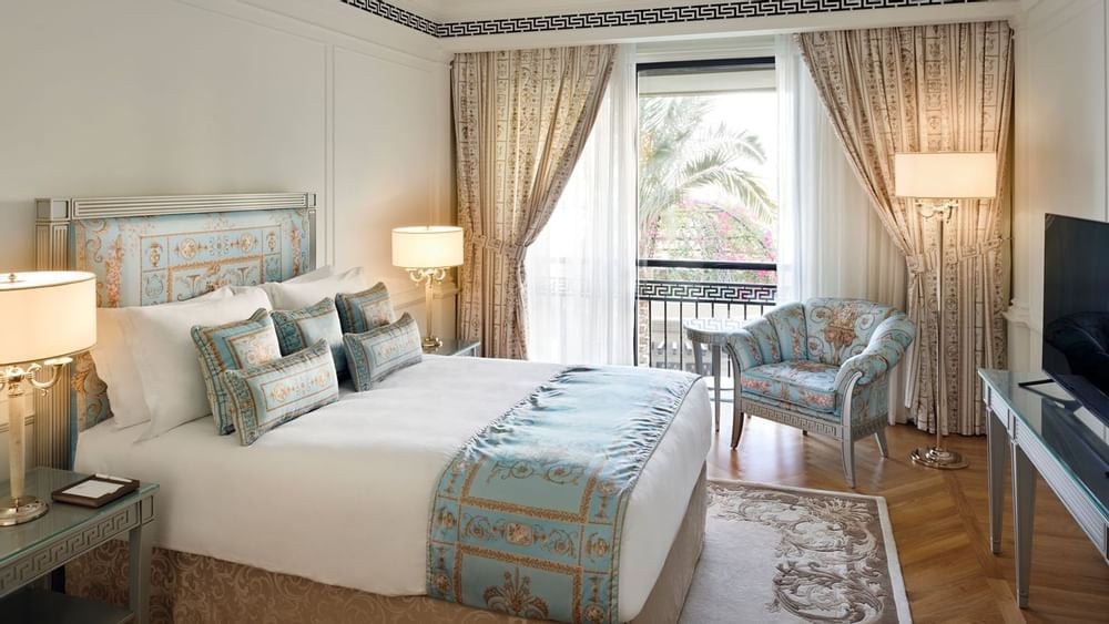 Three-Bedroom Penthouse, bedroom with blue and gold bedding beside a balcony window, at Palazzo Versace Dubai.