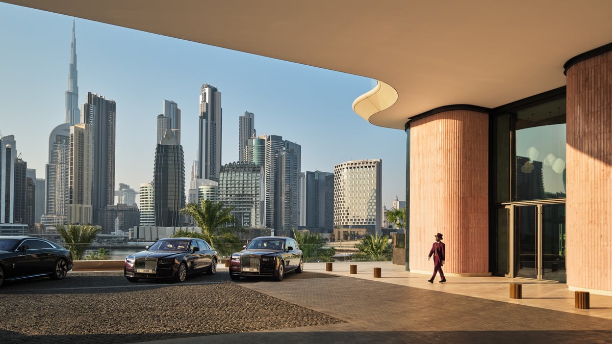 Entrance of The Lana with a doorman walking past parked Rolls-Royces and the Burj Khalifa beyond.