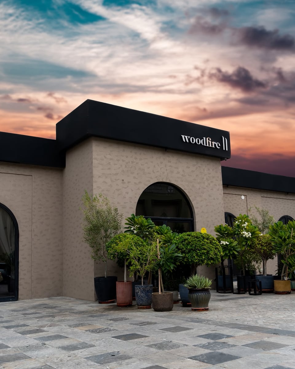 11 Woodfire's pale stone façade and arched doorway under a dusk sky, potted olive and citrus trees along the front