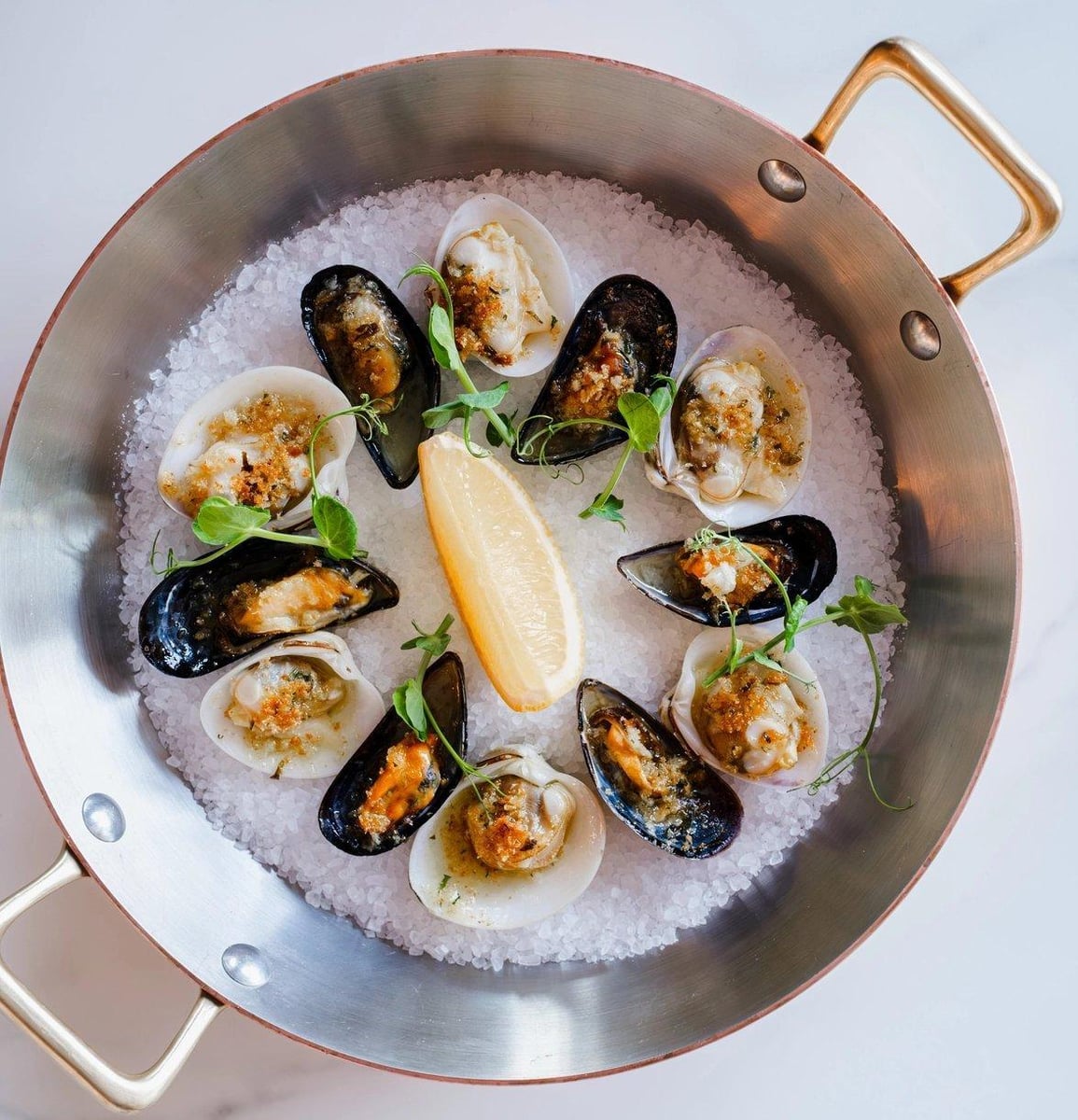 Baked mussels and clams on salt in a copper pan with a lemon wedge