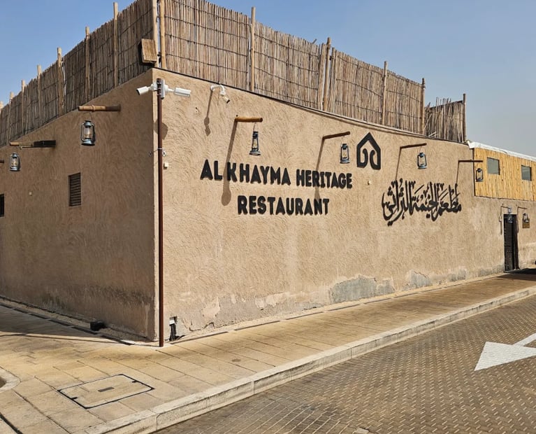 The sand-colored outer wall of Al Khayma Heritage Restaurant with its sign