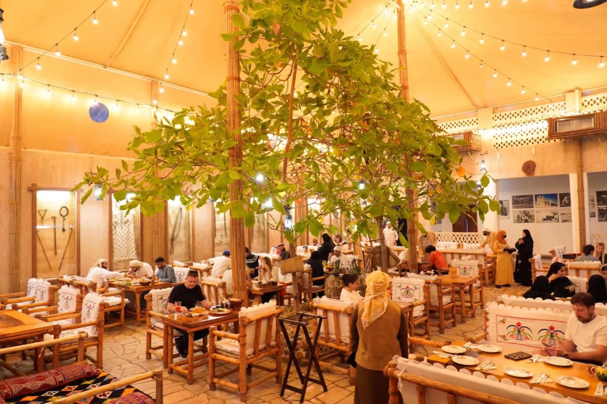 Diners at wooden tables under strings of lights and a shady tree in the tented courtyard