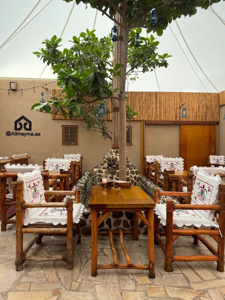 Al Khayma Heritage's courtyard, wooden tables and embroidered chairs around a tree