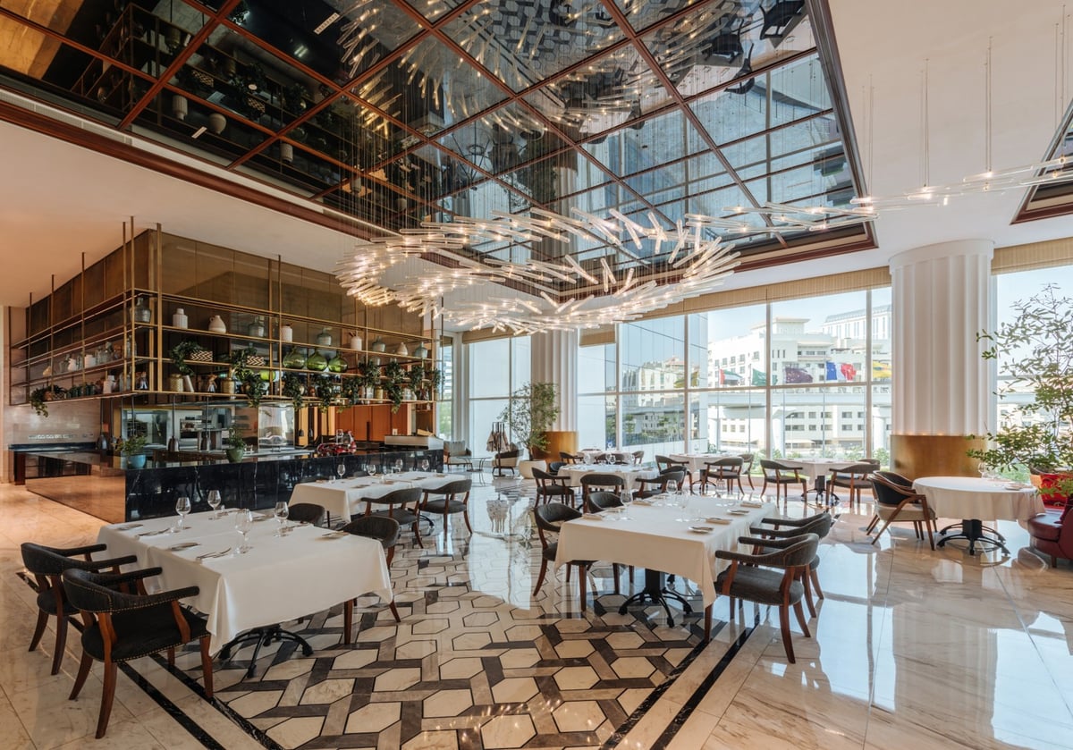 White-clothed tables on a geometric marble floor beside floor-to-ceiling windows, shelves of glassware behind
