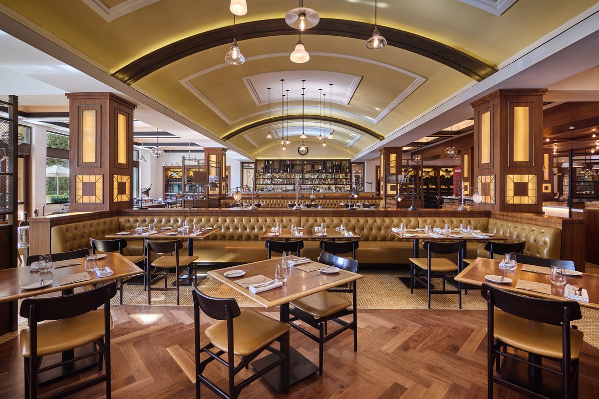 Tables and leather banquettes under a vaulted ceiling with globe pendants, lit wooden pillars along the room