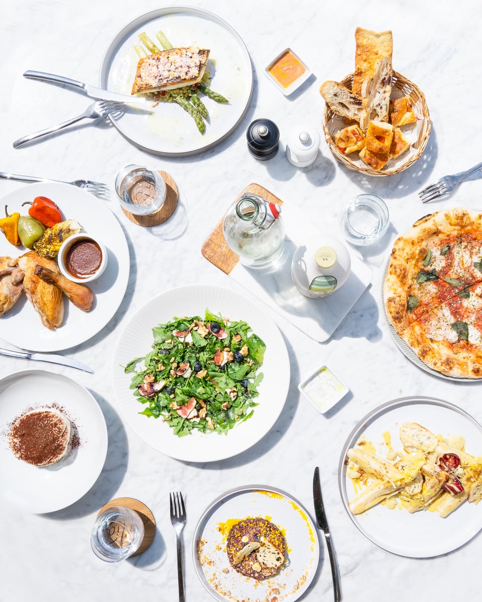 An overhead view of a table spread with pizza, salads, pasta, croquettes and tiramisu