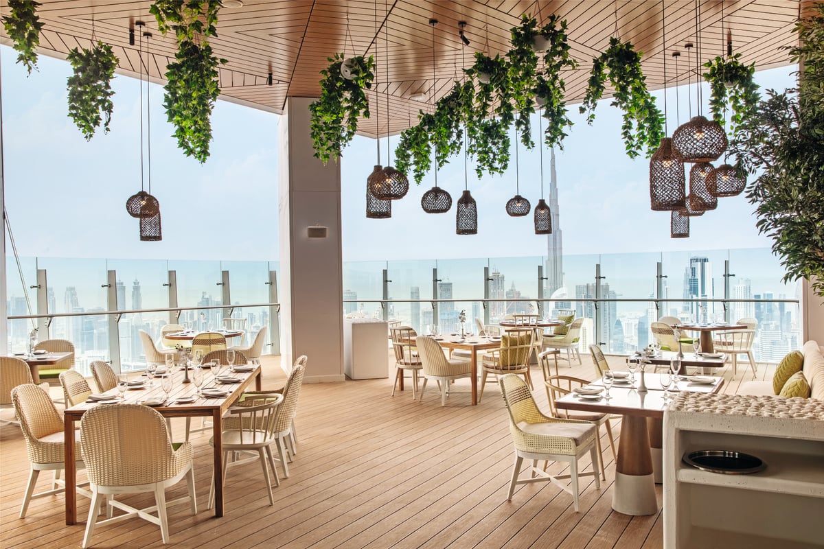 Terrace tables under hanging greenery and woven lanterns, the glass balustrade looking out over the city
