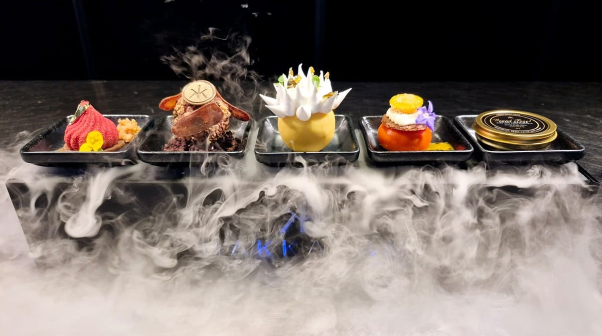 A row of small dim sum dishes on a dark tray over drifting dry-ice mist