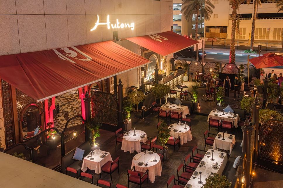 Tables laid in white under red awnings on the terrace, the Hutong sign above