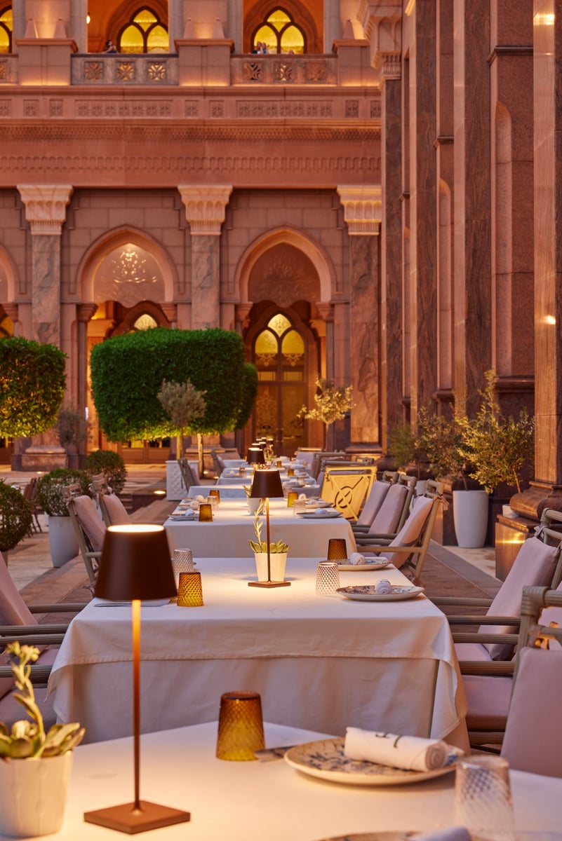 Terrace tables lit by small lamps at dusk beneath the palace's carved, lantern-lit arches