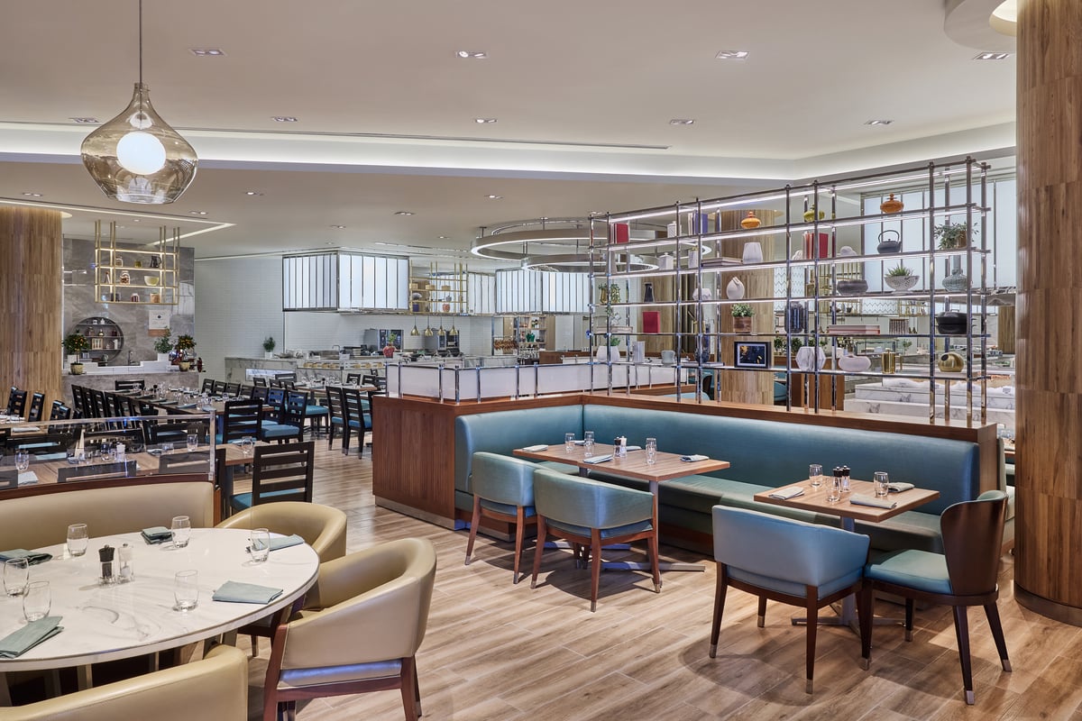 Teal banquettes and round tables beside a tall open shelving wall, the buffet counters beyond