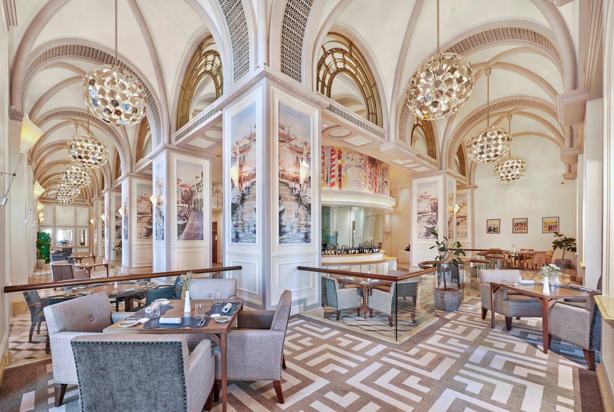 Gray armchairs at laid tables beneath white Gothic vaulting and glittering globe chandeliers