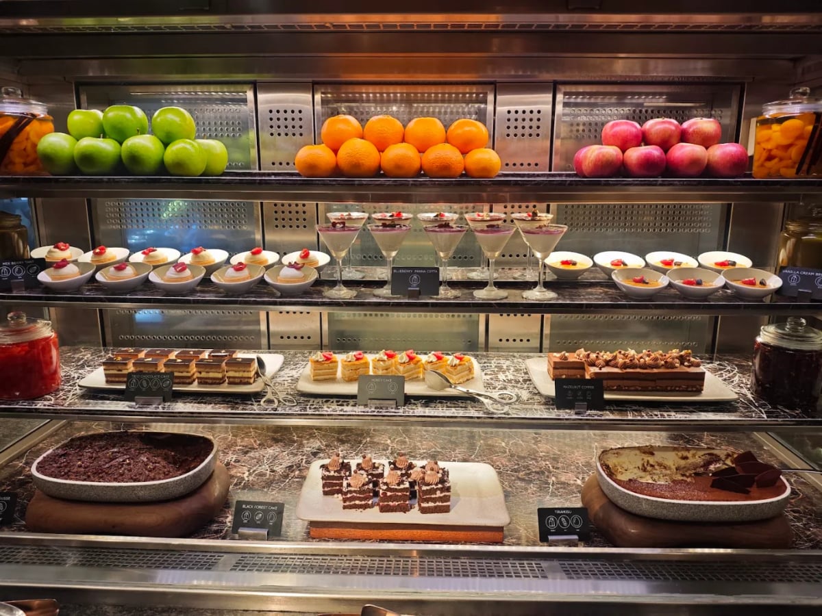 A glass cabinet of fresh fruit, small desserts and cakes on three tiers