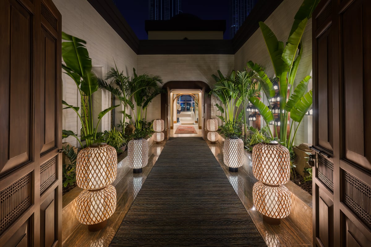 A long dark walkway lined with lanterns and banana plants leading to Thiptara's doors