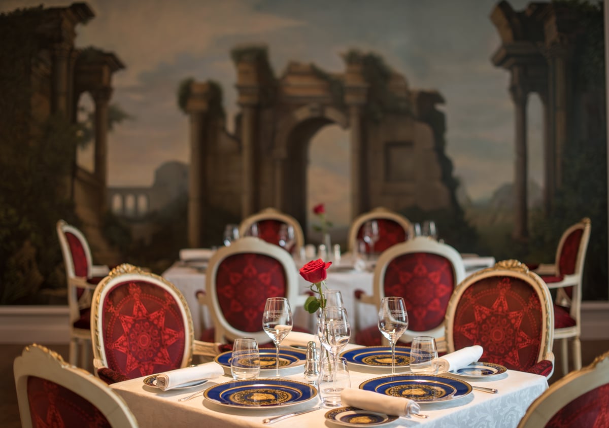 A table set with Versace-pattern plates and a red rose in front of the classical mural